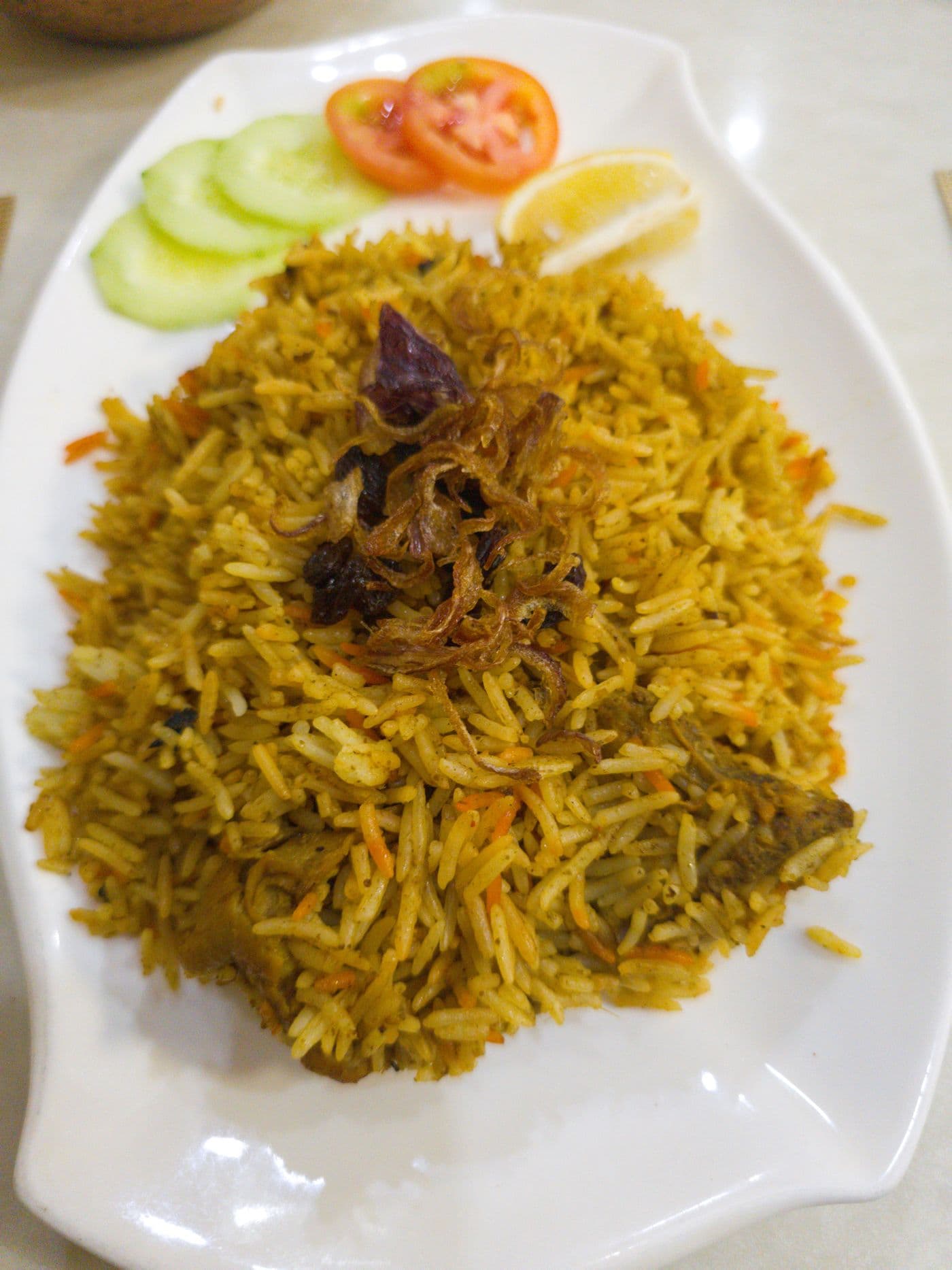 Chicken Biryani garnished with fried onions, cucumber, tomato, and lemon